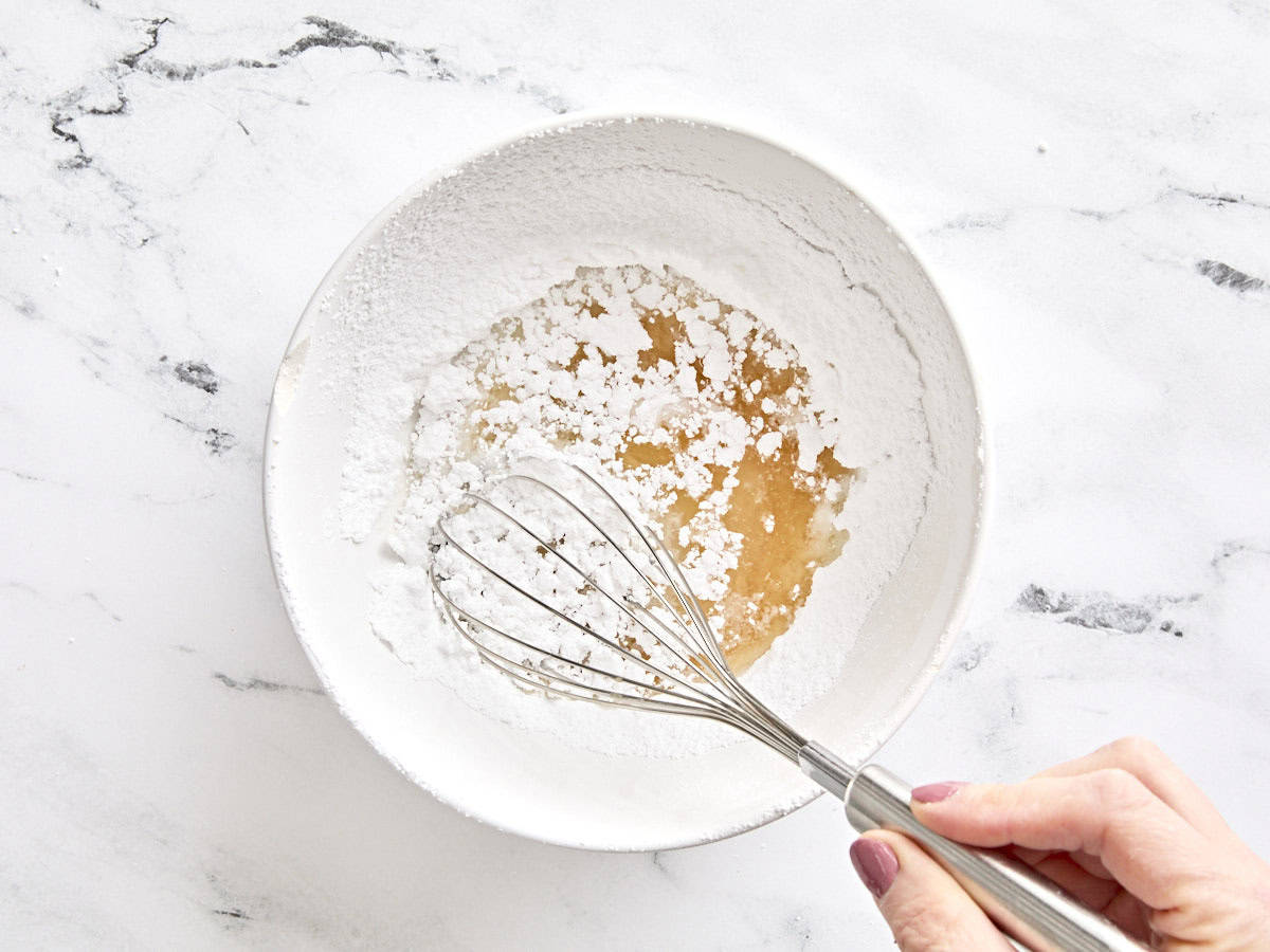 Corn syrup, lemon juice, and hot water being whisked into powdered sugar in a bowl.