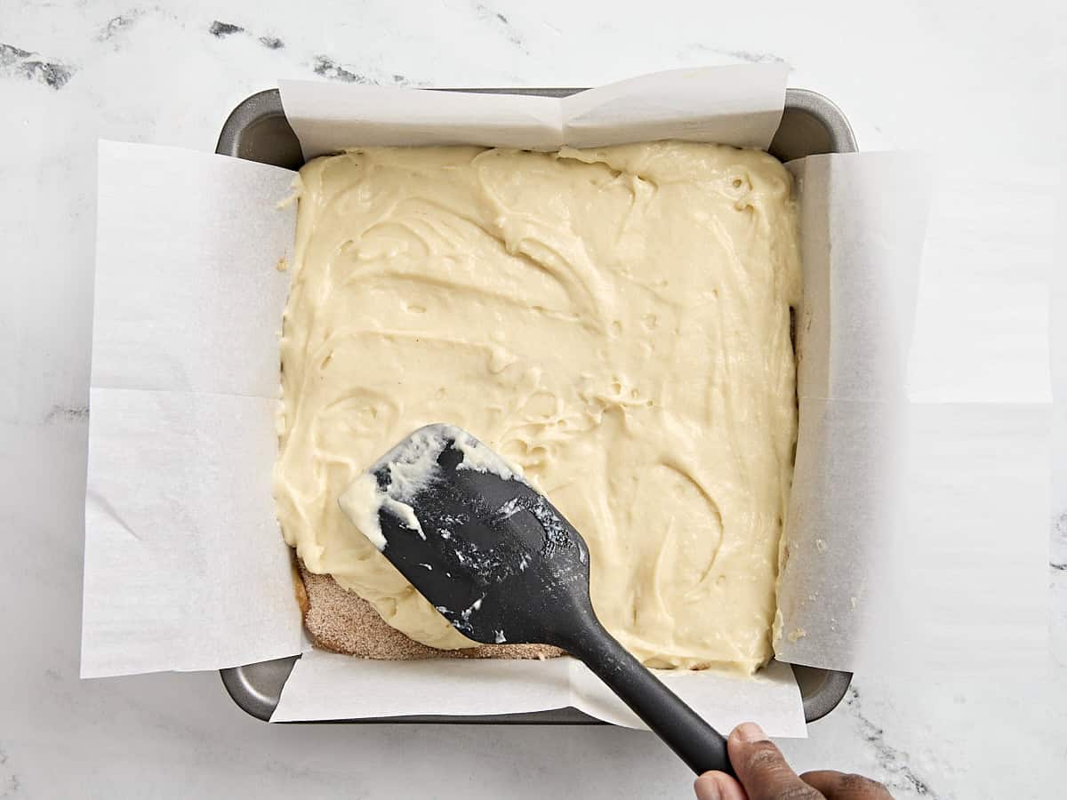 A spatula spreading the top layer of coffee cake batter in a parchment lined baking dish.