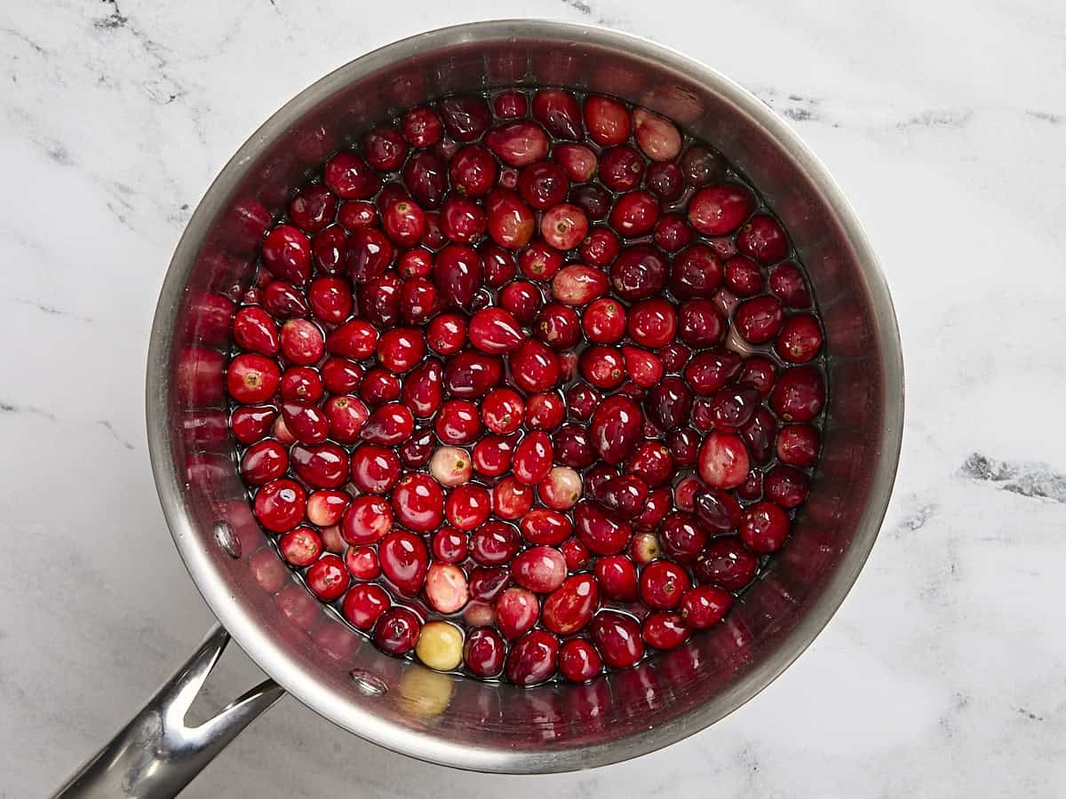 Fresh cranberries in a pan of sugar water.