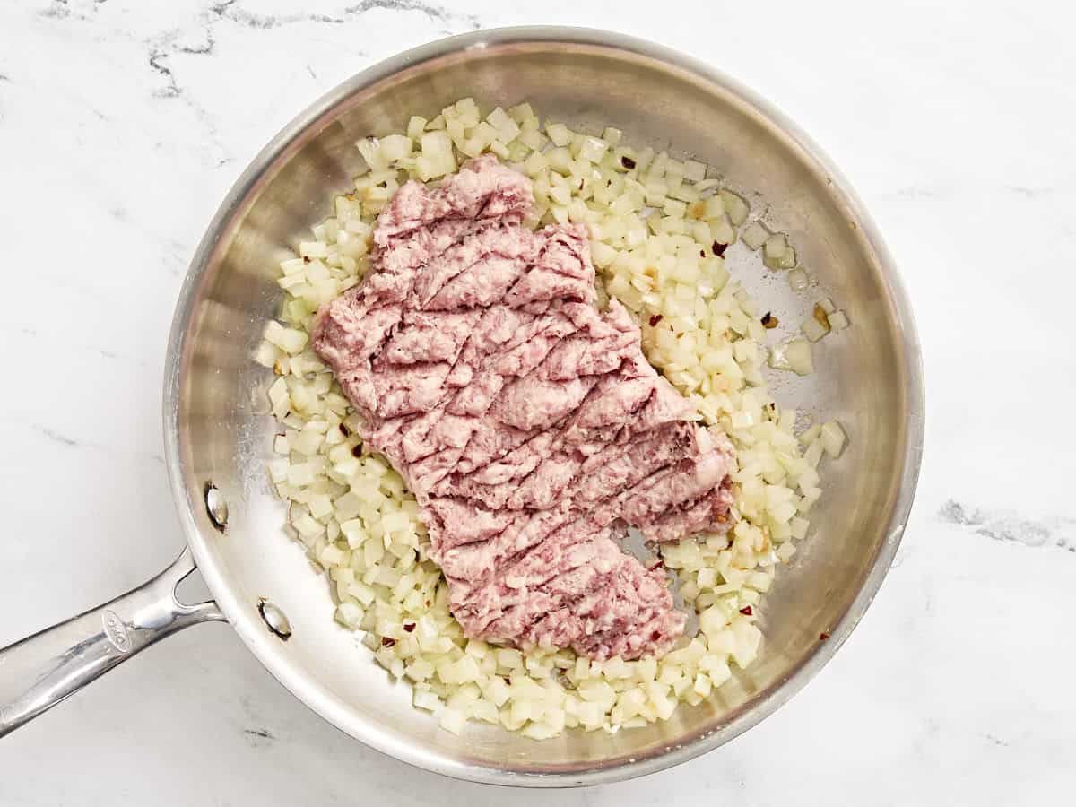 Ground sausage added to a skillet with diced onions.