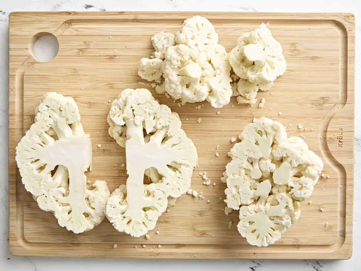 Cauliflower steaks on a wooden chopping board.