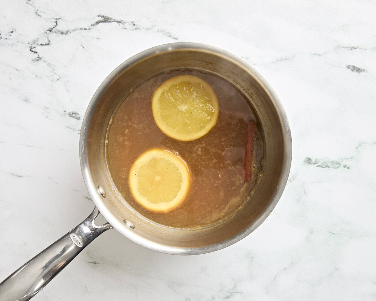 Hot apple cider in a pan with sliced oranges and a cinnamon stick.