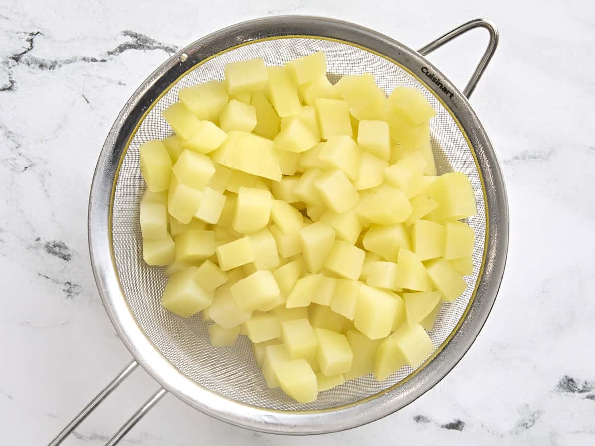 Parboiled diced potatoes in a strainer.