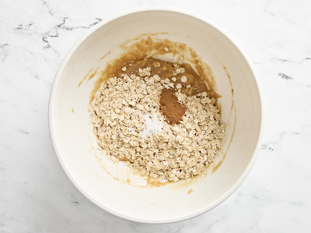 Oats and salt added to the wet ingredients for breakfast cookies in a mixing bowl.