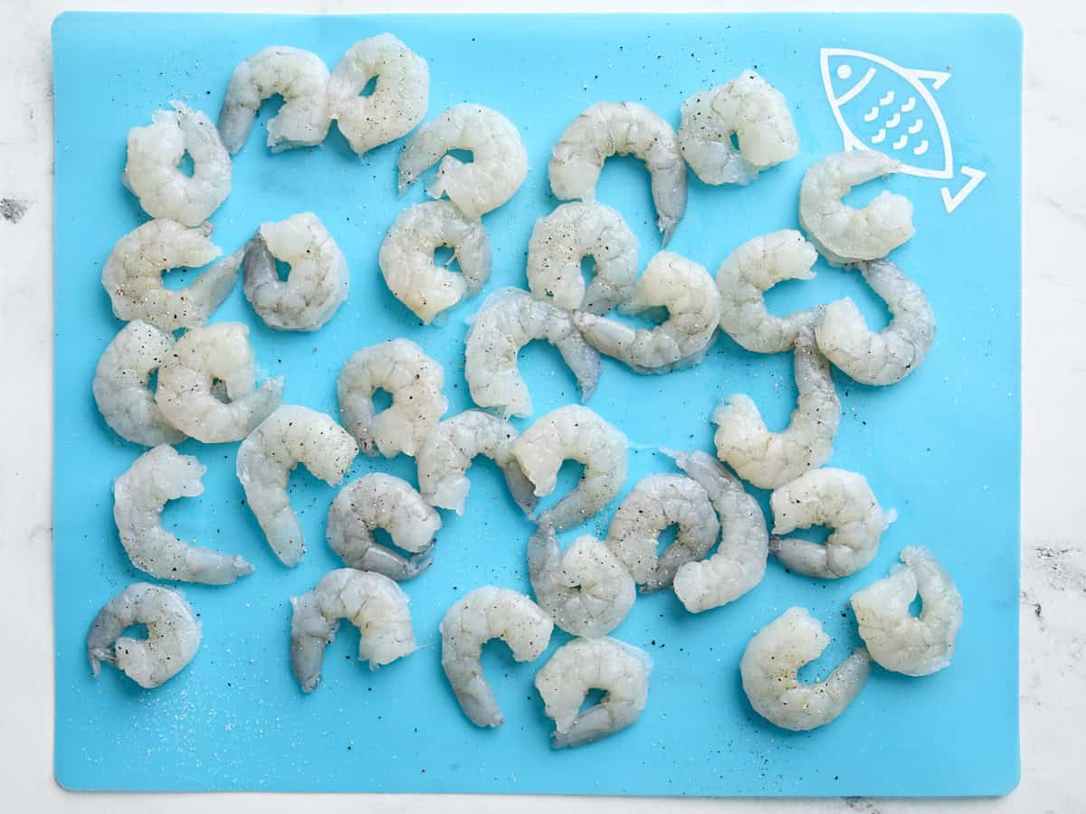 Seasoned raw shrimps on a seafood preparation mat.