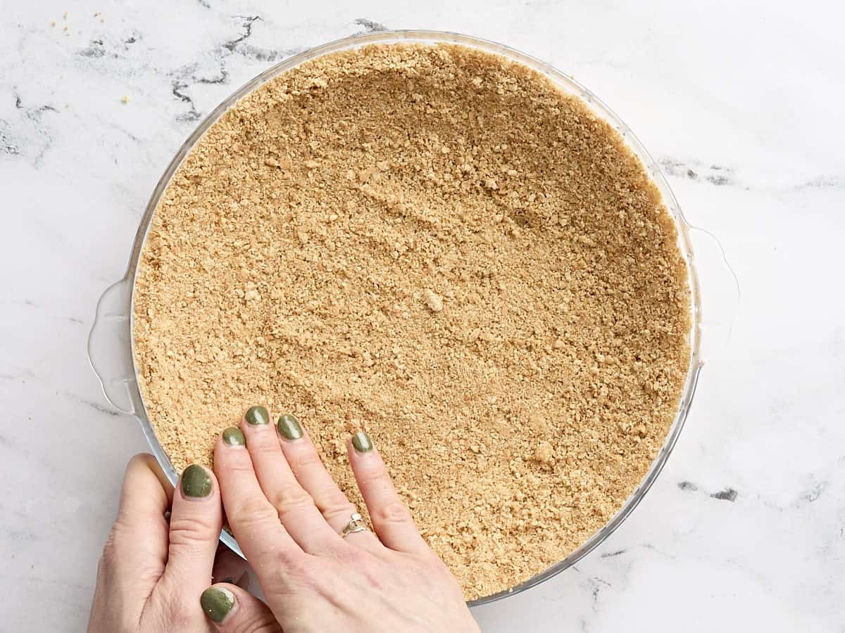 A hand pressing graham cracker crumbs into a food processor.