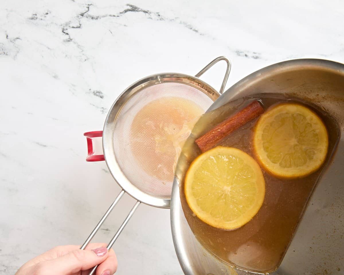 Hot cider being poured out a pan into a strainer.