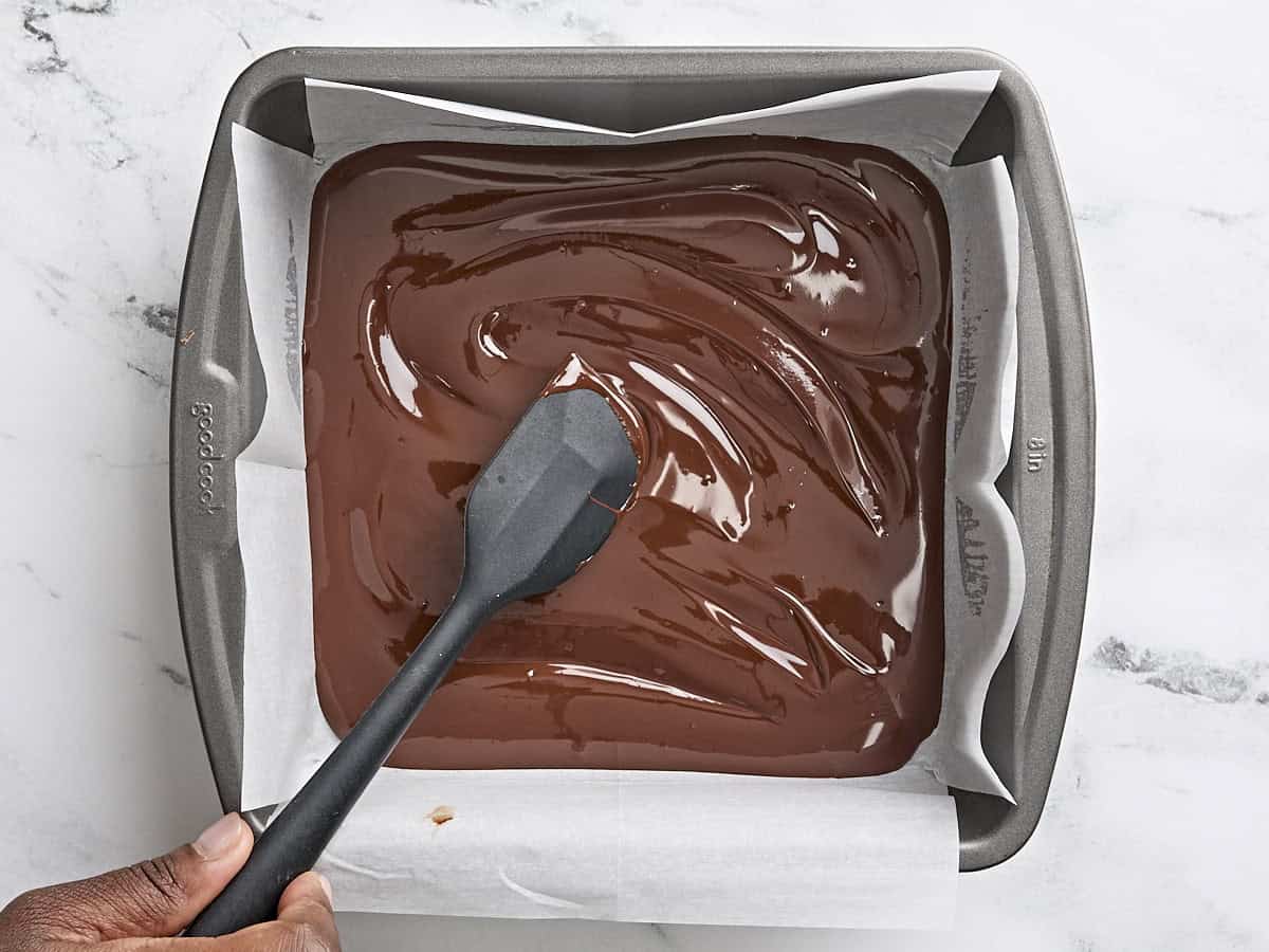 A spatula spreading out melted chocolate in a parchment lined baking sheet.