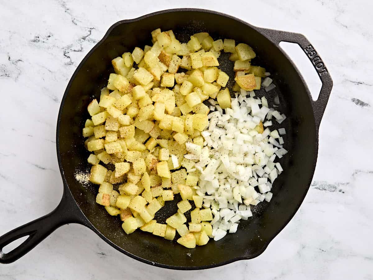 Diced onion added to skillet breakfast potatoes in a skillet.