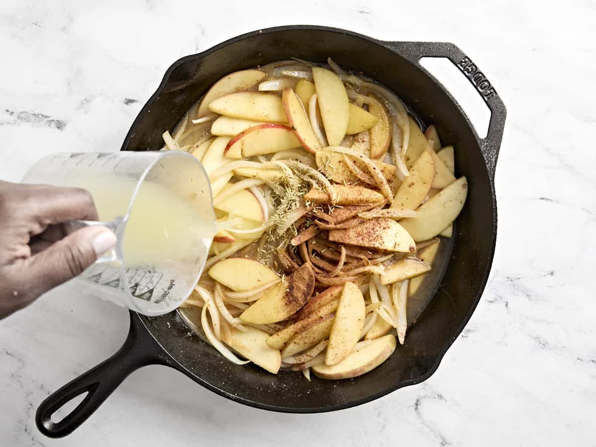 Chicken broth and being poured into a skillet with seasonings and sliced apples and onions.