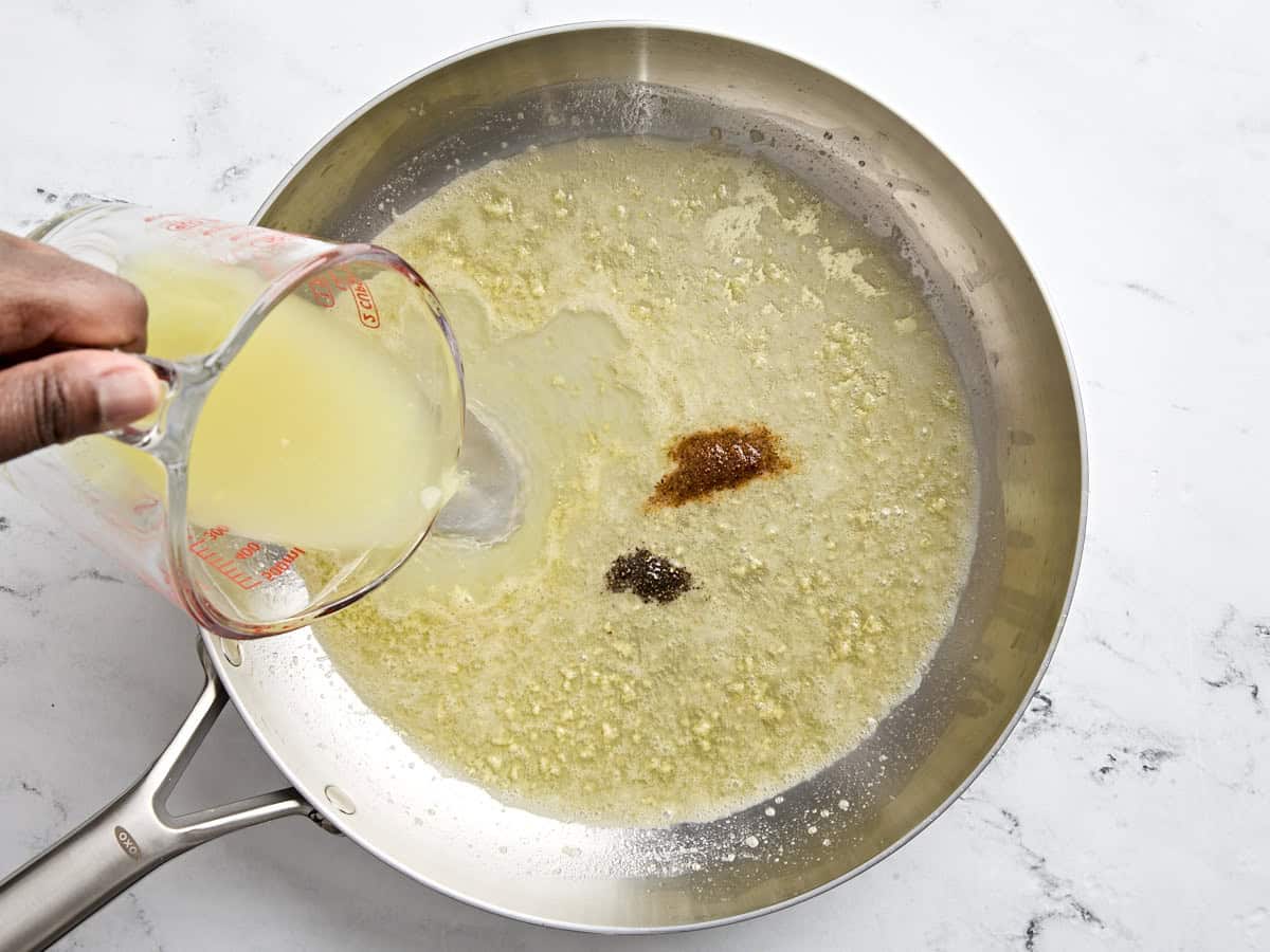 Chicken broth and seasonings added to garlic butter in a skillet.