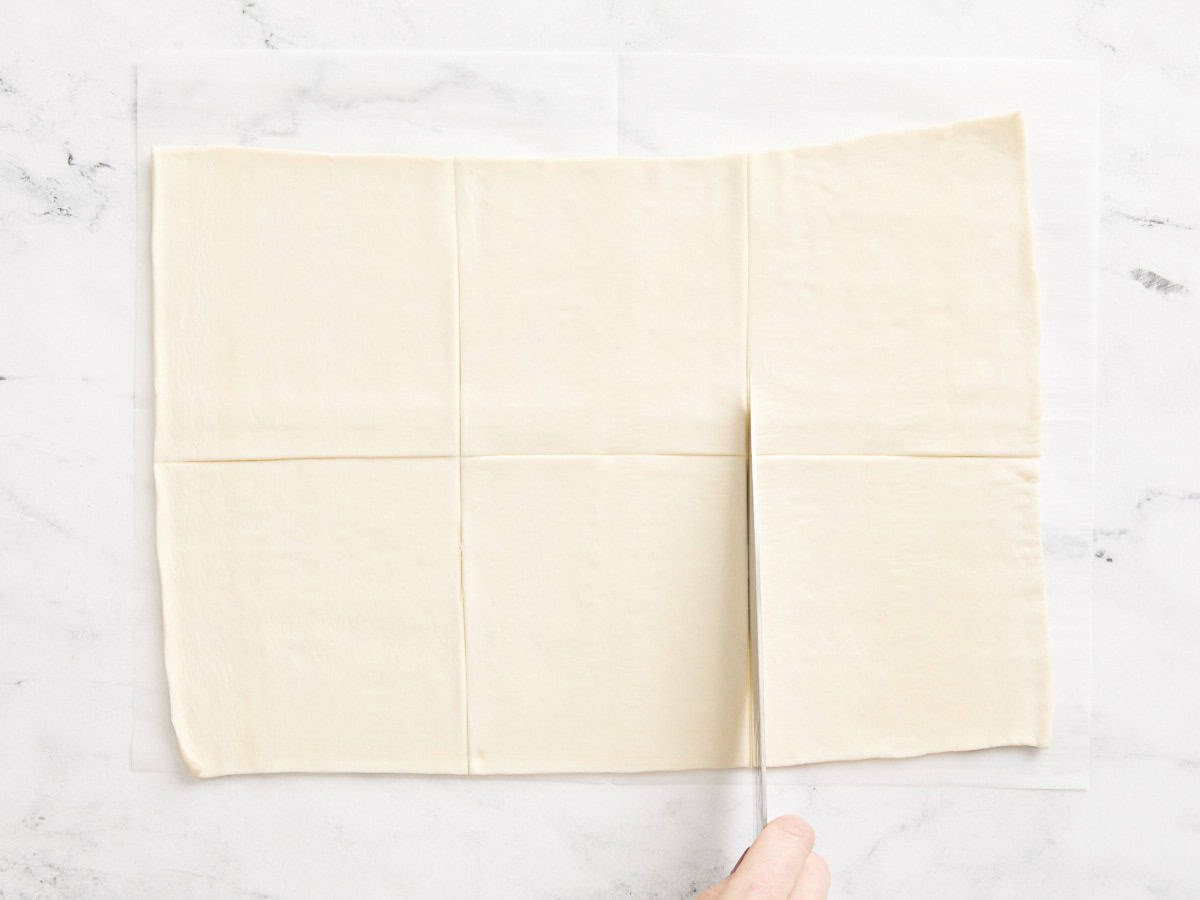 A knife cutting a sheet of puff pastry into square.