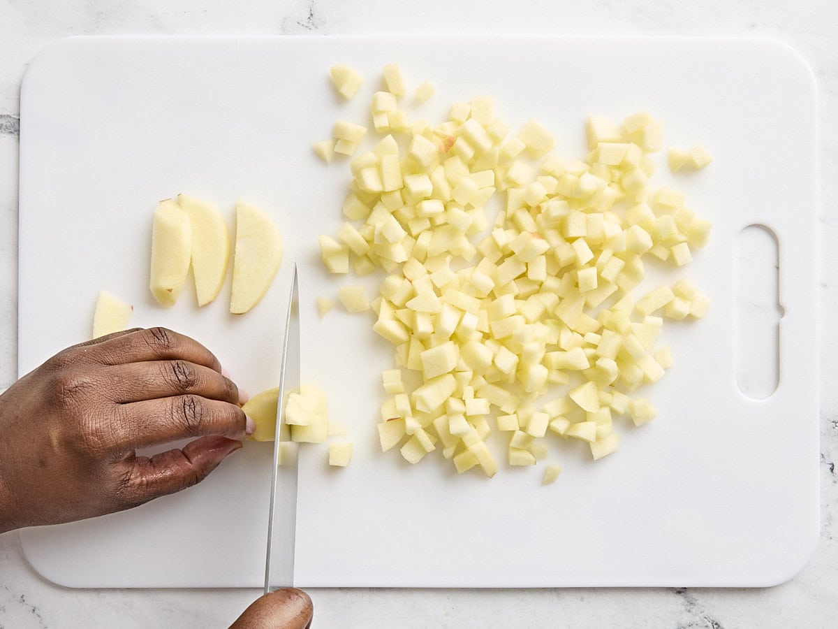 A hand dicing apples on a white chopping board.