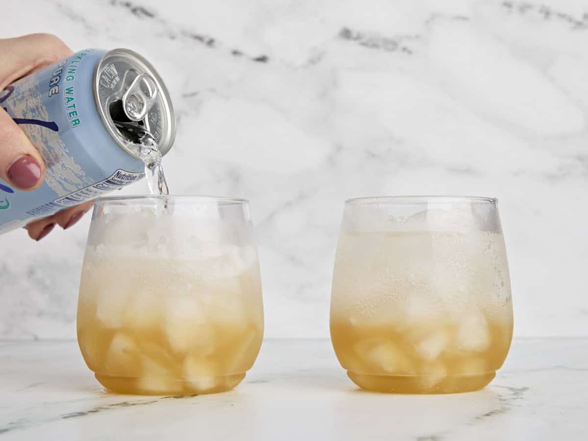 Soda water being pour into a glass of ice with apple cider shrub to make a mocktail.