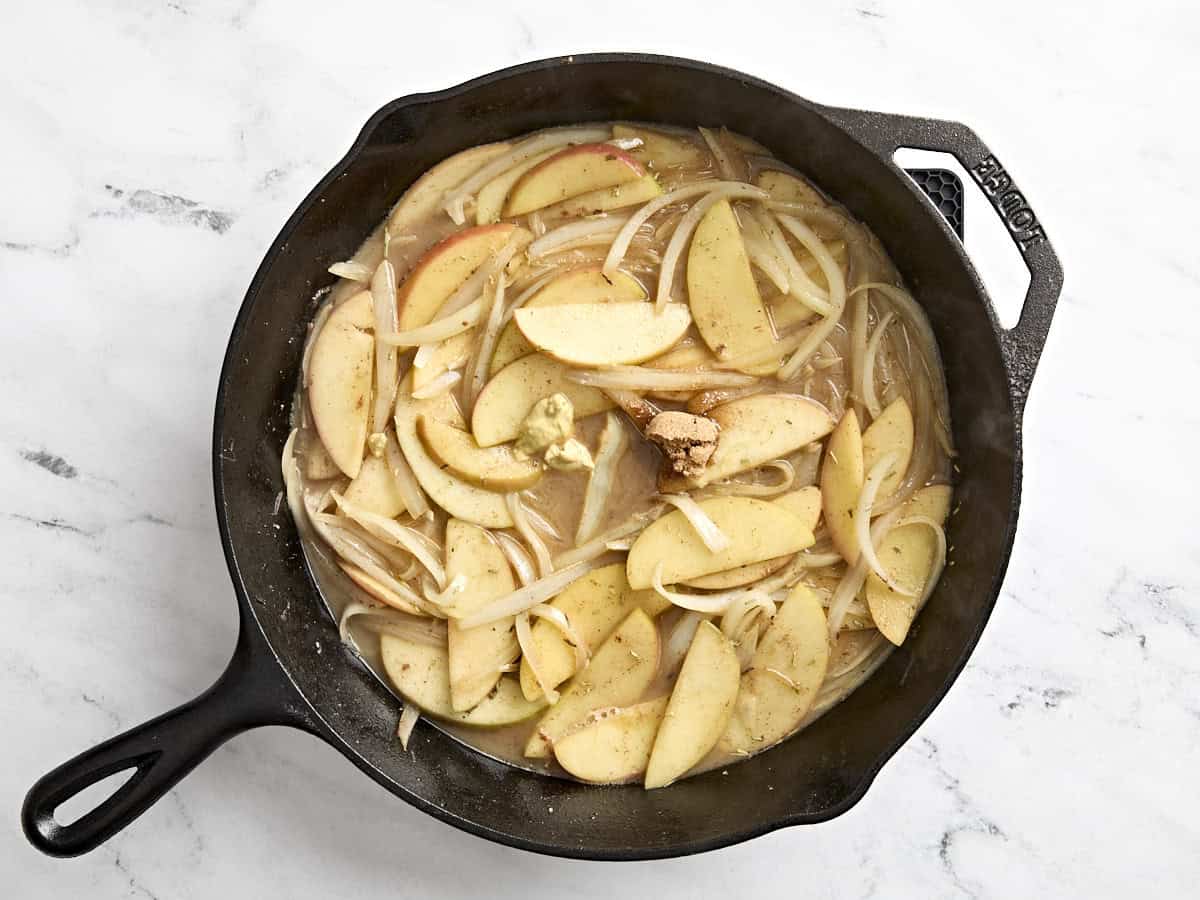 Sliced apples and onions cooking in a apple cider sauce in a skillet.