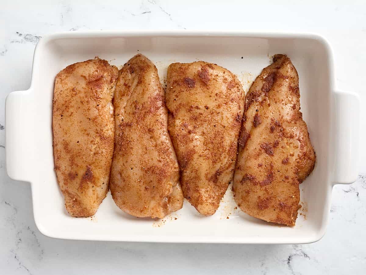 Four seasoned chicken breasts in a baking dish.