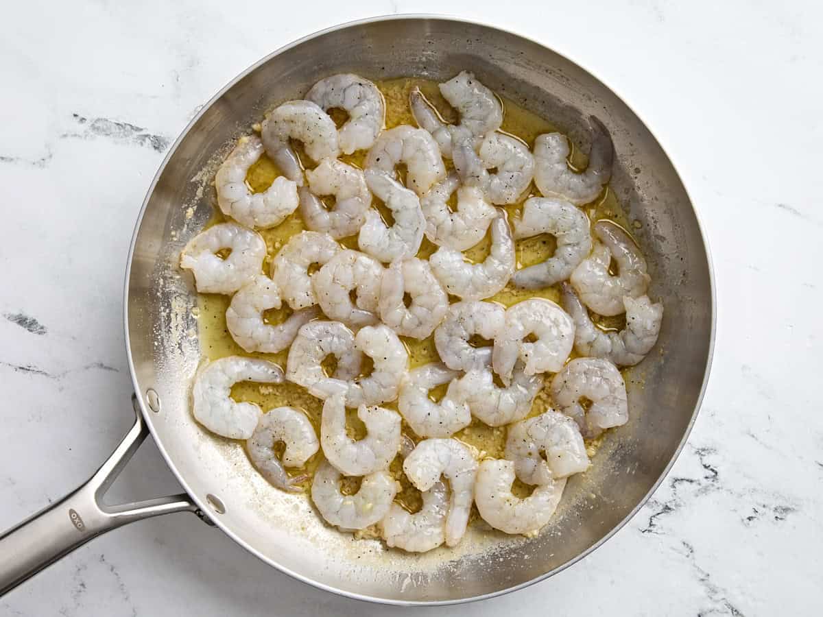 Raw shrimps added to garlic butter sauce in a skillet to make shrimp scampi.