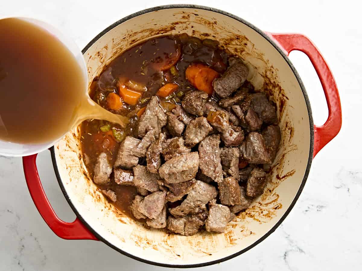 Broth being poured over beef stew in a dutch oven.