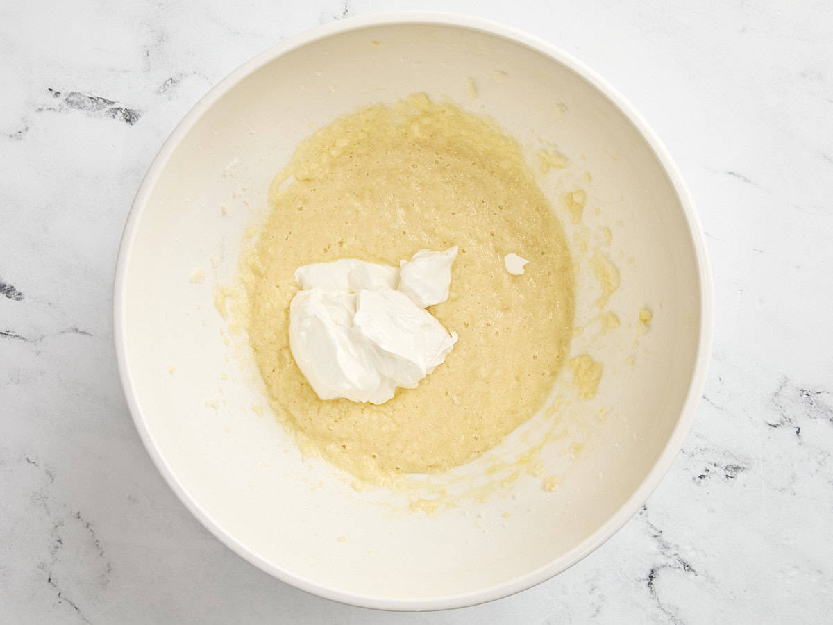 Sour cream added to the wet ingredients for coffee cake in a mixing bowl.