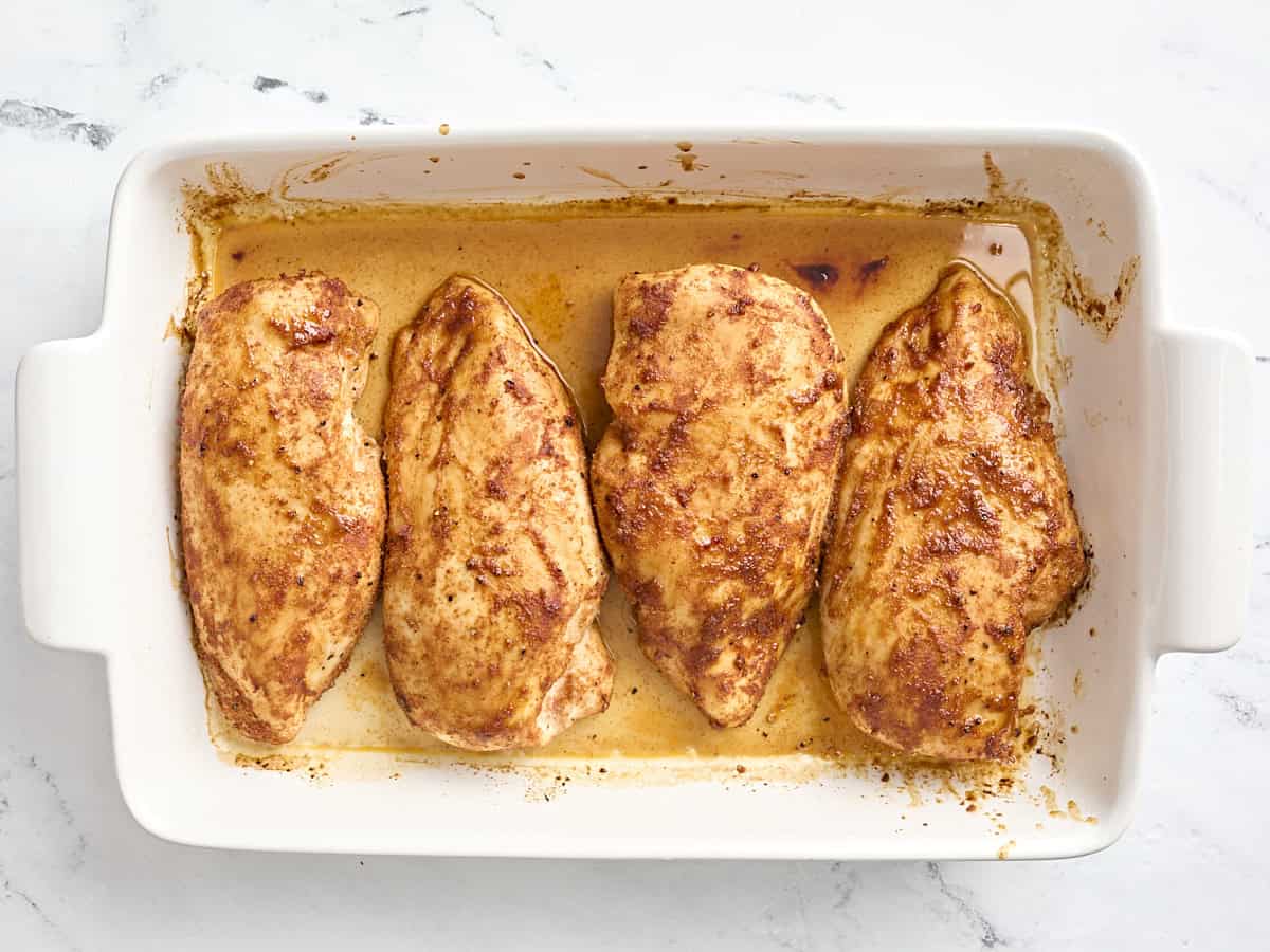 Four baked chicken breasts in a baking dish.