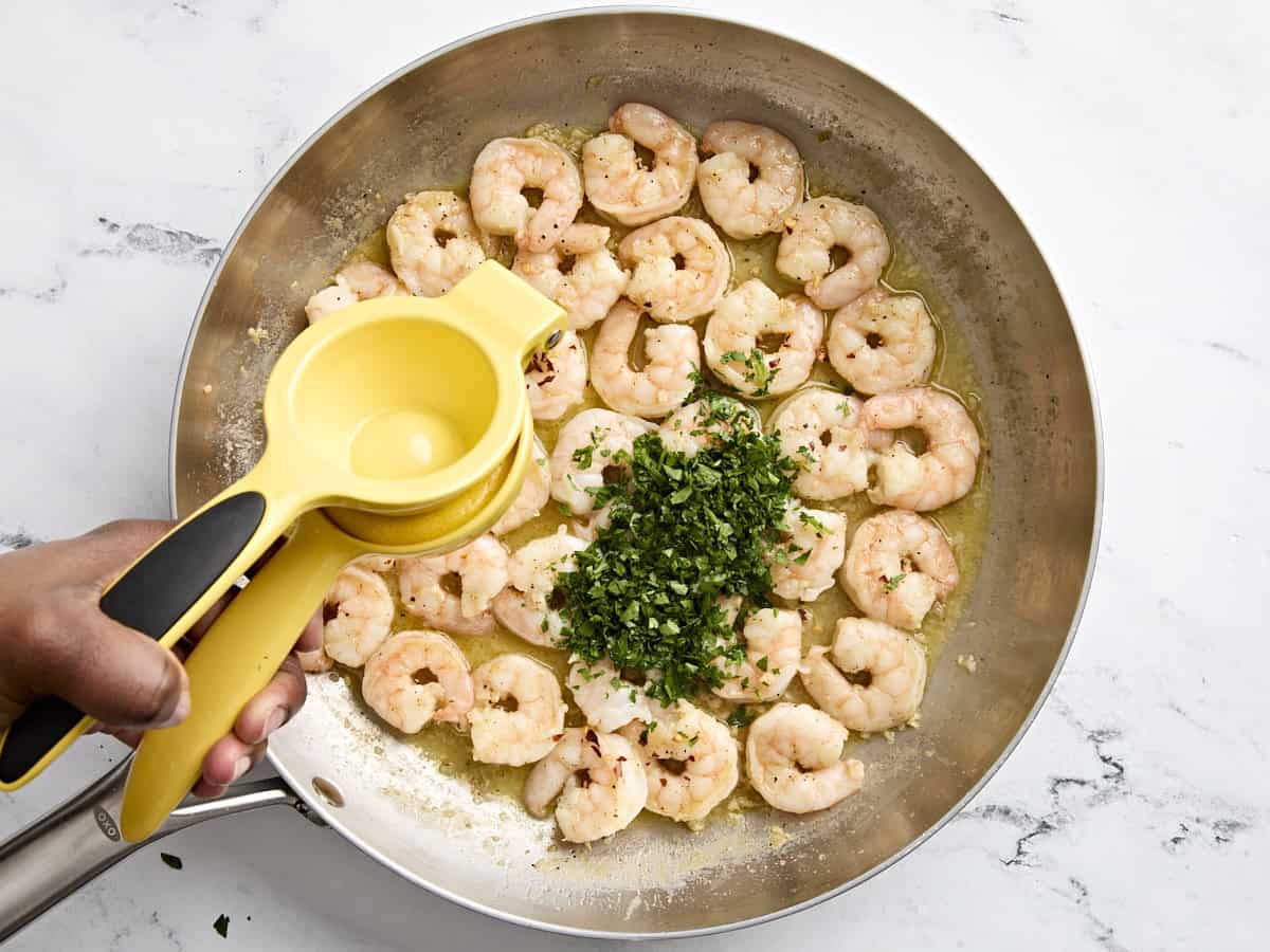 Half a lemon being squeezed into shrimp scampi, with fresh parsley added.