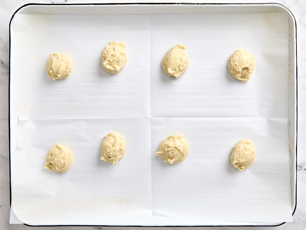 Scoops of black and white cookie dough on a parchment lined baking sheet.