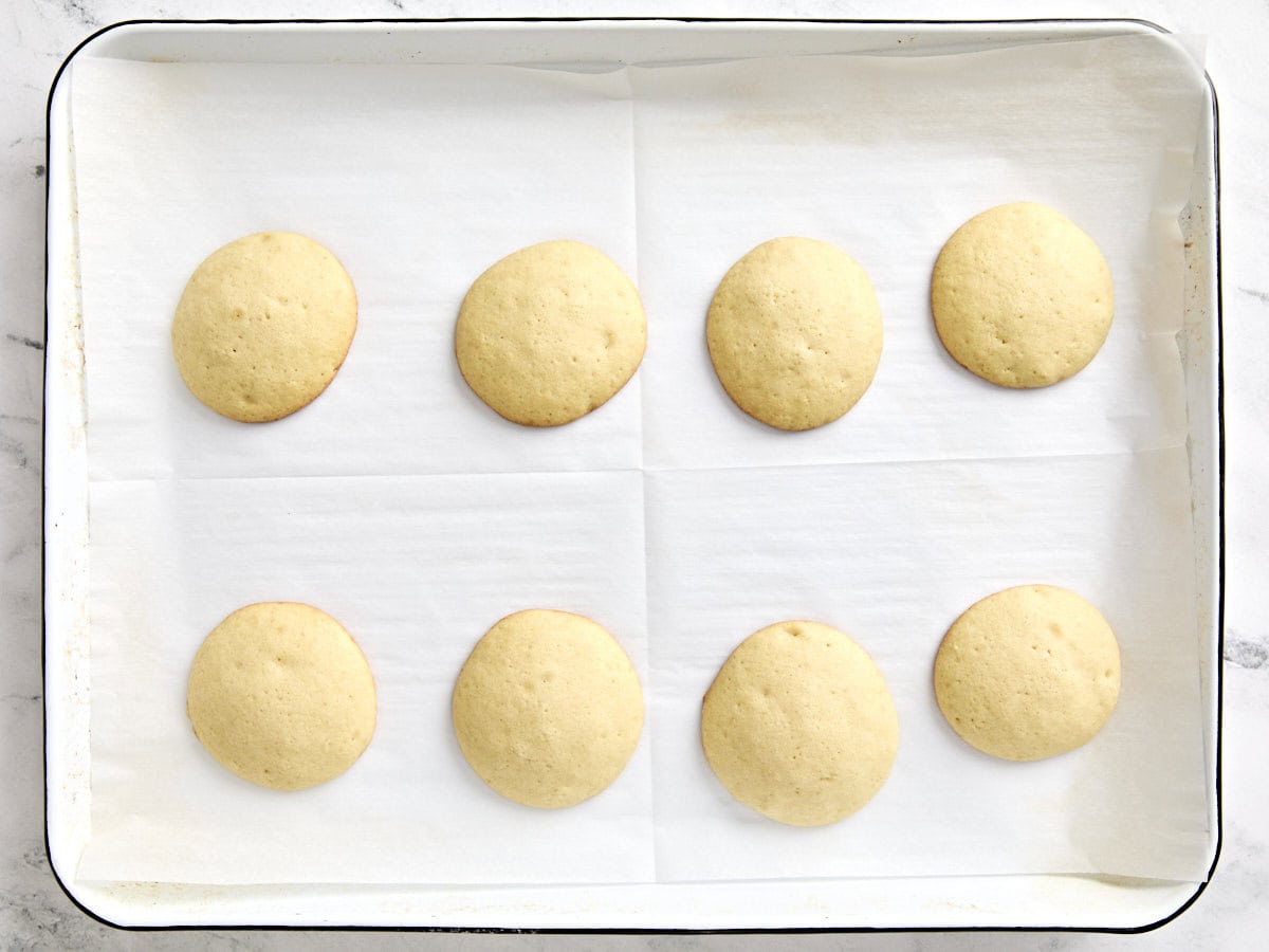 Unfrosted black and white cookies on a parchment lined baking sheet.