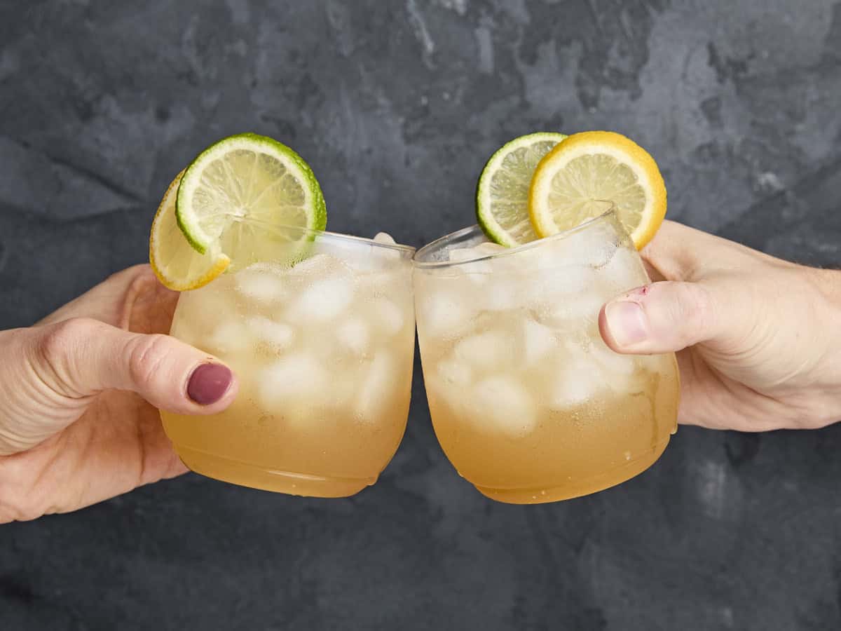 Two hands clinking together two glasses of Apple Cider Shrub Mocktail.