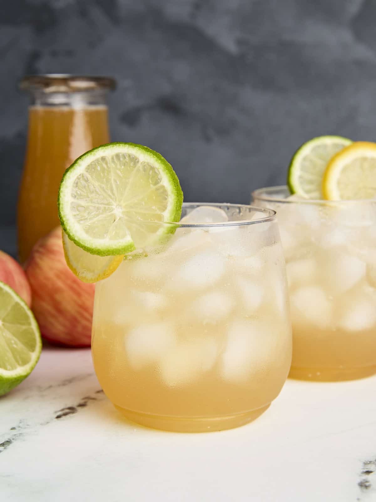 Side view of Apple Cider Shrub Mocktail in glasses, with lemon and lime slices as garnish.