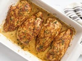 Overhead view of four baked chicken breasts in a baking dish, garnished with fresh parsley.