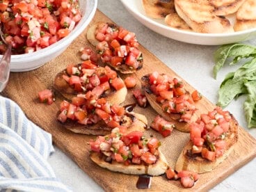 Overhead view of bruschetta on a wooden chopping board with balsamic glaze.