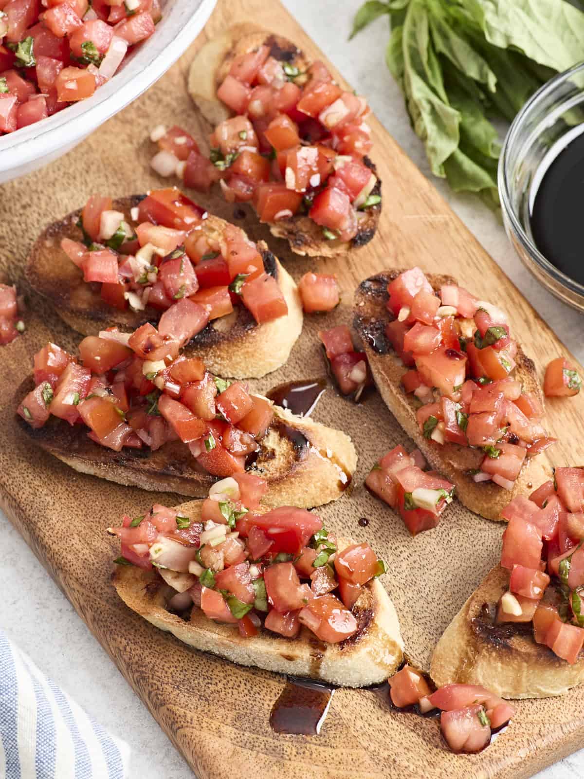 Overhead view of bruschetta on a wooden chopping board with balsamic glaze.