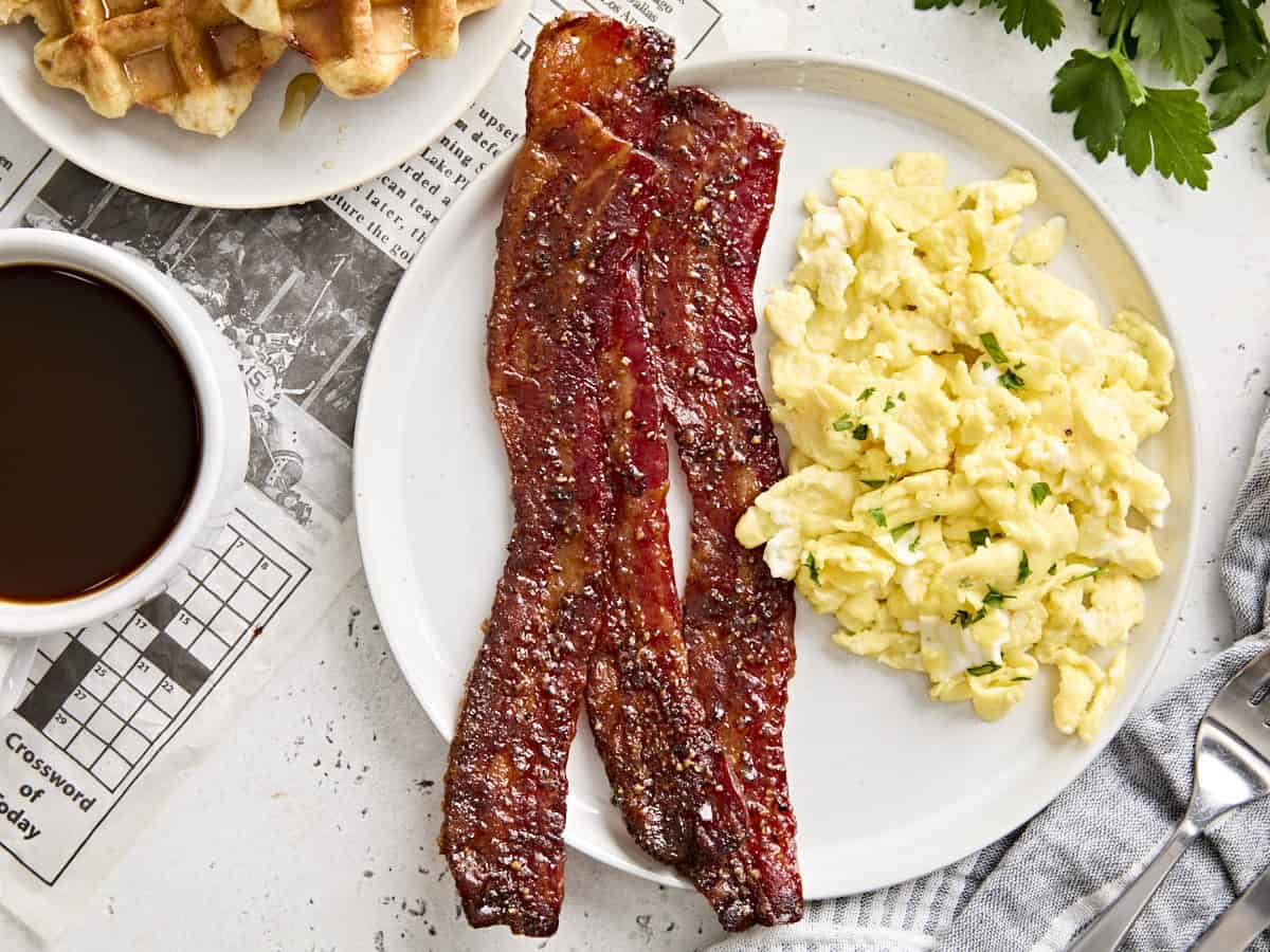 Overhead view of candied bacon and scrambled eggs on a plate.