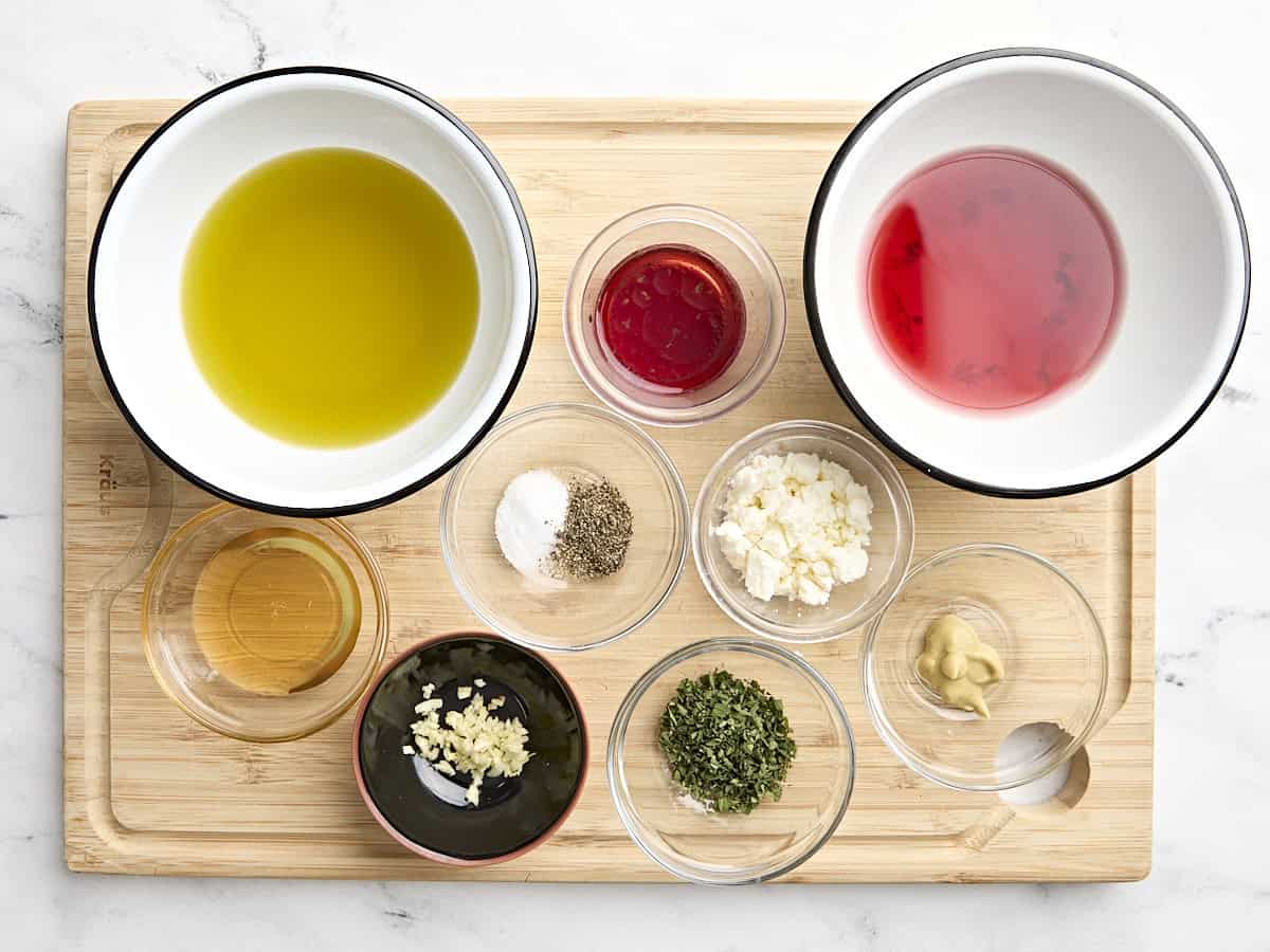 Overhead view of the ingredients for greek salad dressing on a wooden cutting board.