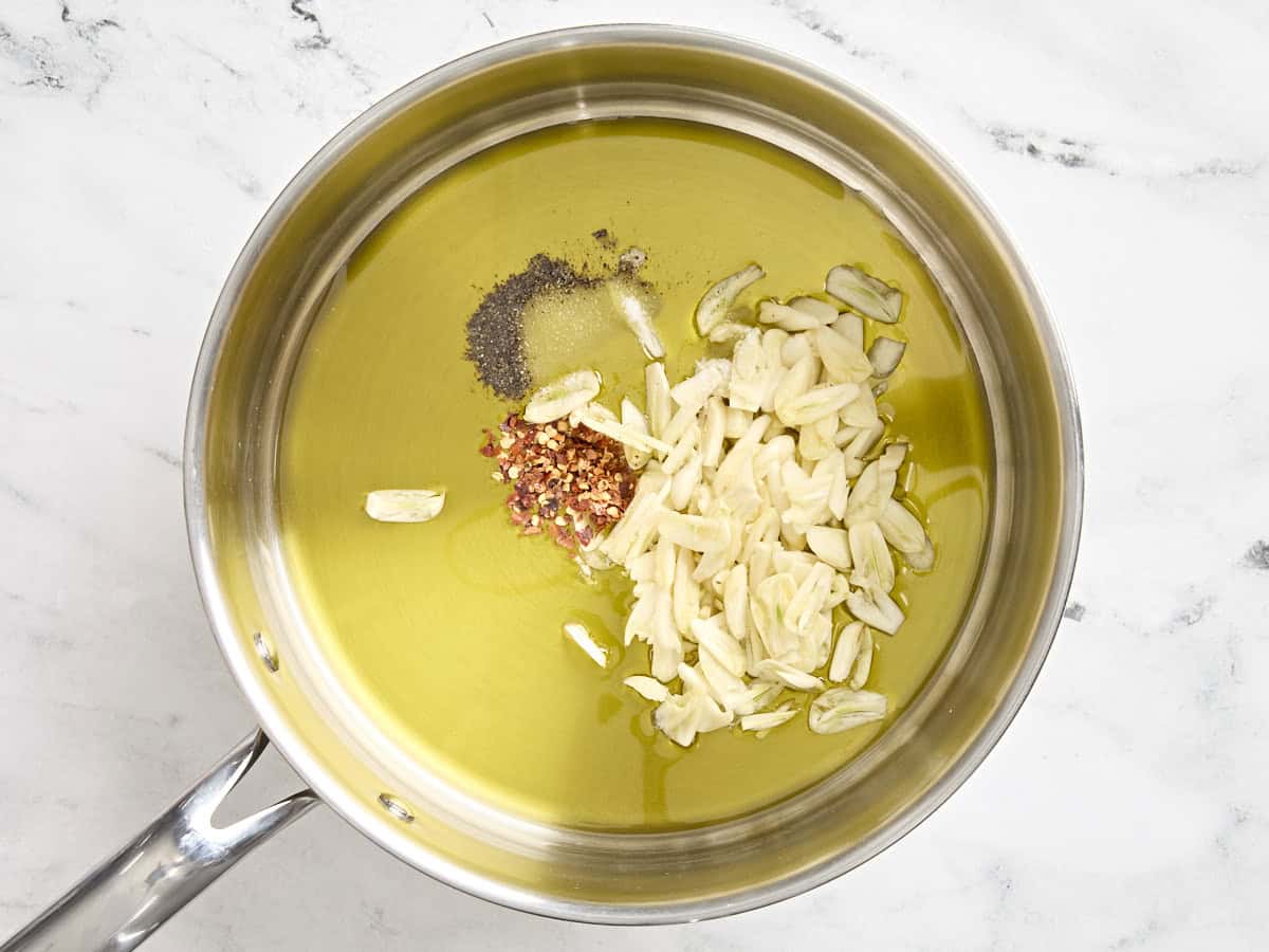 Sliced garlic, black pepper, salt, and red pepper flakes in a saucepan with olive oil.