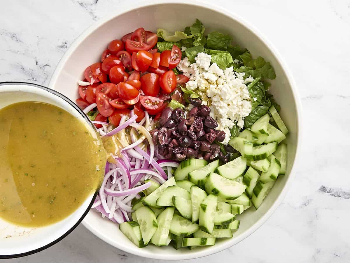 Greek salad dressing being poured into a bowl of greek salad.