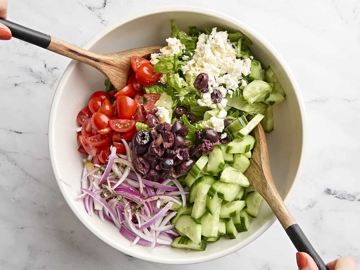 Greek salad being tossed in a bowl.