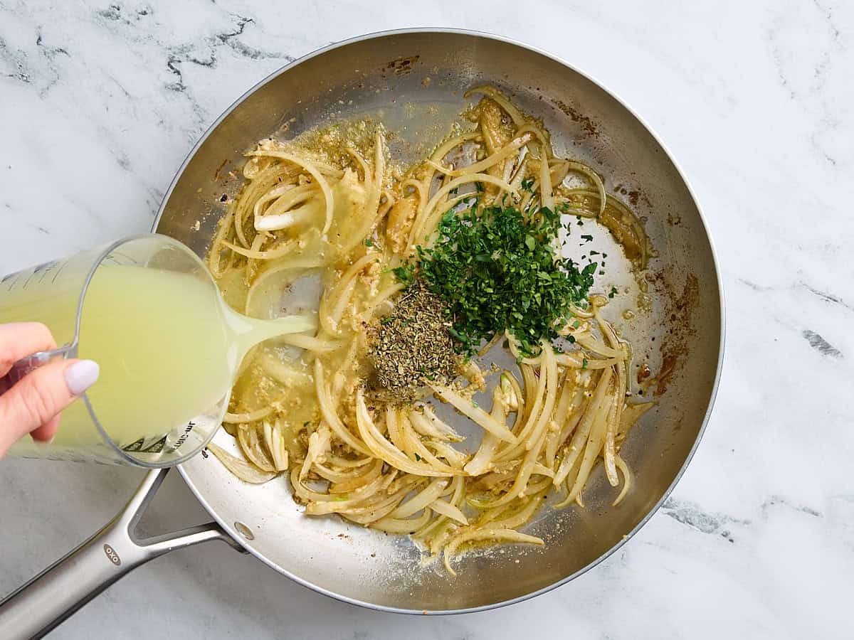 Chicken broth being poured into a skillet with sauteed onions, garlic, and seasonings.
