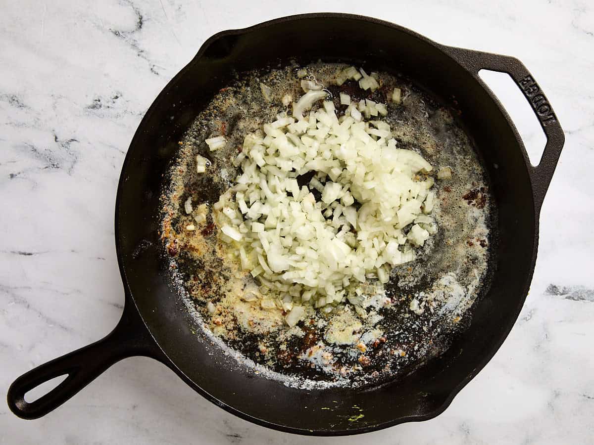 Diced onion cooking in melted butter in a cast iron skillet.