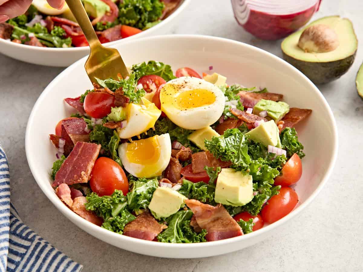 Side view of a finished BLAT salad bowl with a fork taking some.