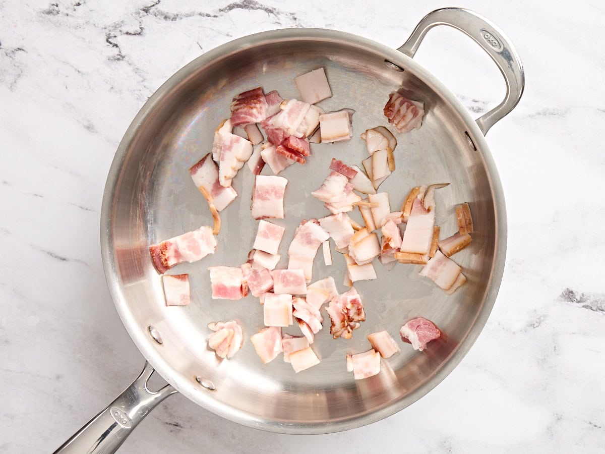 Bacon lardons cooking in a skillet.